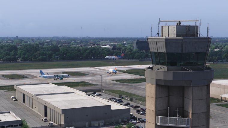A control tower beside a hangar, with airliners on the apron behind it.